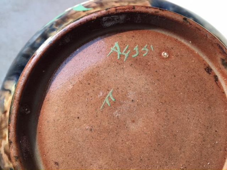 May include: Close-up of the bottom of a brown ceramic bowl with a green glaze. The bowl has a blue and brown design on the outside. The bottom is marked with the text "A4351" and a green "T".