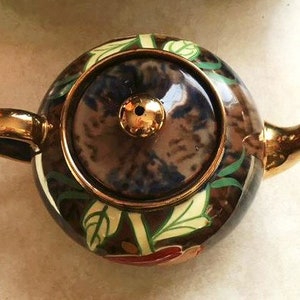 May include: A brown and gold teapot with a floral design. The teapot has a lid with a blue and white pattern. The teapot is decorated with gold accents.