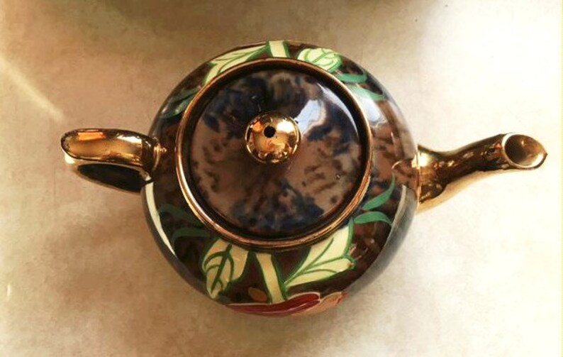 May include: A brown and gold teapot with a floral design. The teapot has a lid with a blue and white pattern. The teapot is decorated with gold accents.