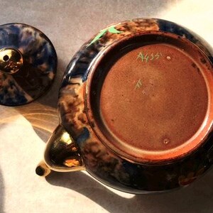 May include: A blue and brown teapot with gold accents and a lid. The bottom of the teapot has the number "A435" written on it.