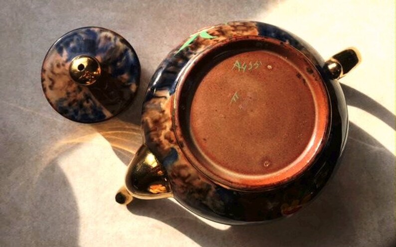 May include: A blue and brown teapot with gold accents and a lid. The bottom of the teapot has the number "A435" written on it.