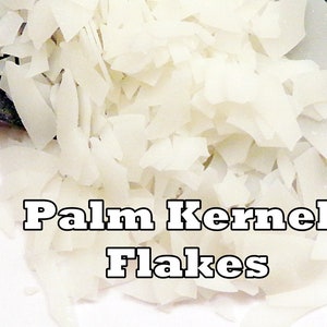 May include: Close-up of a pile of white palm kernel flakes. The flakes are irregularly shaped and appear to be dry. The text "Palm Kernel Flakes" is displayed in a bold, outlined font.