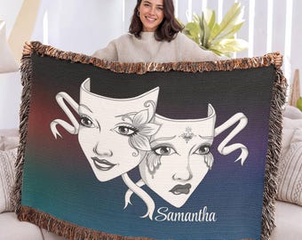 May include: A woven throw blanket featuring a gradient background transitioning from black to blue. The design displays two theatrical masks with white faces and black line art details, accompanied by the name Samantha in white script.