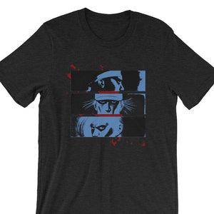 May include: A dark heather grey t-shirt with a graphic print of three men's faces in black and white with blue and red accents. The faces are in a row, with the top face wearing a hat.