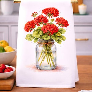 May include: White kitchen towel featuring a watercolor illustration of red geranium flowers in a clear glass jar. The flowers have green leaves and are tied with twine. The towel is hanging on a gold bar.