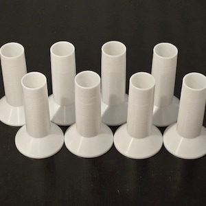 May include: Eight white plastic bobbins with a flared base. The bobbins are all the same size and shape.