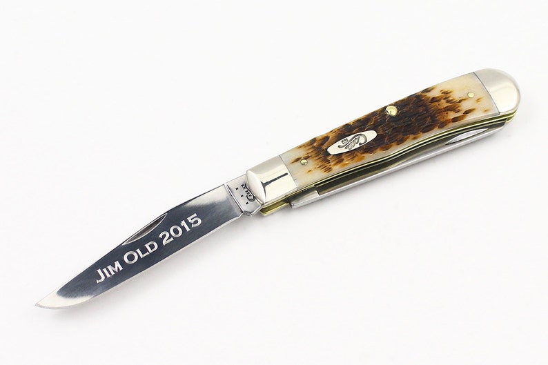 May include: A silver pocket knife with a brown and white handle. The blade is open and engraved with the text "JIM OLD 2015".