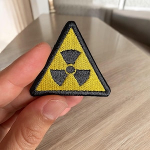 May include: Embroidered yellow and black radiation hazard patch. The triangular patch features a yellow background with a black radiation symbol in the center. The patch is outlined with a black border.