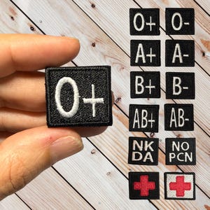 May include: A set of black and white embroidered patches with different blood types, including O+, O-, A+, A-, B+, B-, AB+, AB-, NK DA, NO PCN, and two red crosses.