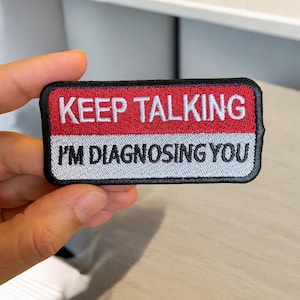 May include: A red and gray embroidered patch with black stitching. The patch reads "KEEP TALKING I'M DIAGNOSING YOU".