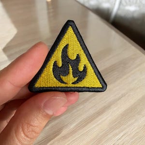 May include: Yellow triangle warning patch with a black flame symbol. The patch is embroidered and has a black border.
