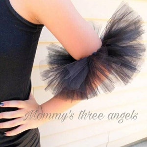 May include: Black tulle arm cuff with a ruffled design. The cuff is made of soft, delicate tulle and is perfect for adding a touch of elegance to any outfit.