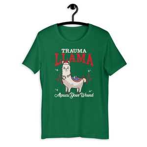 K&ouml;nnte beinhalten: Gr&uuml;nes T-Shirt mit kurzen &Auml;rmeln mit einem Cartoon-Lama, das eine Krankenschwesterm&uuml;tze und ein Stethoskop tr&auml;gt. Der Text "Trauma Llama" befindet sich &uuml;ber dem Lama und "Alpaca Your Wound" unter dem Lama.