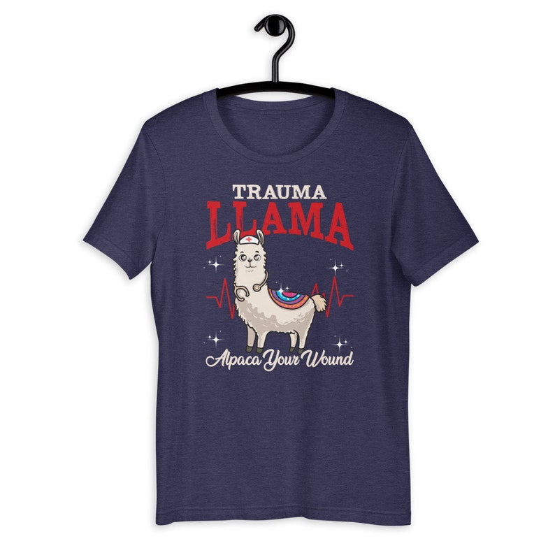 K&ouml;nnte beinhalten: Ein marineblaues T-Shirt mit einem Cartoon-Lama, das eine Krankenschwesterm&uuml;tze und ein Stethoskop tr&auml;gt. Der Text "Trauma Llama" befindet sich &uuml;ber dem Lama und "Alpaca Your Wound" unter dem Lama.