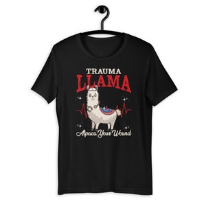 K&ouml;nnte beinhalten: Schwarzes T-Shirt mit einem Cartoon-Lama, das eine Krankenschwesterm&uuml;tze und ein Stethoskop tr&auml;gt. Der Text "Trauma Llama" befindet sich &uuml;ber dem Lama und "Alpaca Your Wound" unter dem Lama.