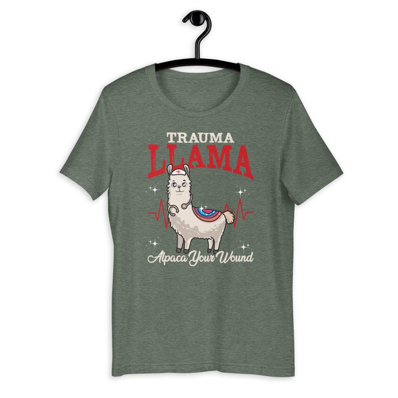 K&ouml;nnte beinhalten: Gr&uuml;nes T-Shirt mit einem Cartoon-Lama, das eine Krankenschwesterm&uuml;tze und ein Stethoskop tr&auml;gt. Der Text "Trauma Llama" befindet sich &uuml;ber dem Lama und "Alpaca Your Wound" unter dem Lama.