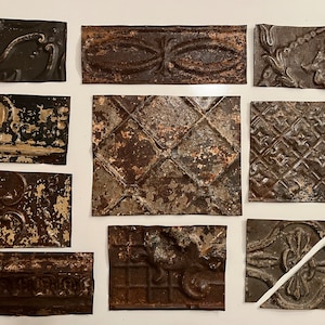 May include: An assortment of antique, weathered tin ceiling tiles in various geometric and floral patterns. The tiles are primarily shades of brown and gray, with visible signs of age and wear, suggesting a vintage aesthetic. Some tiles are square, others rectangular.