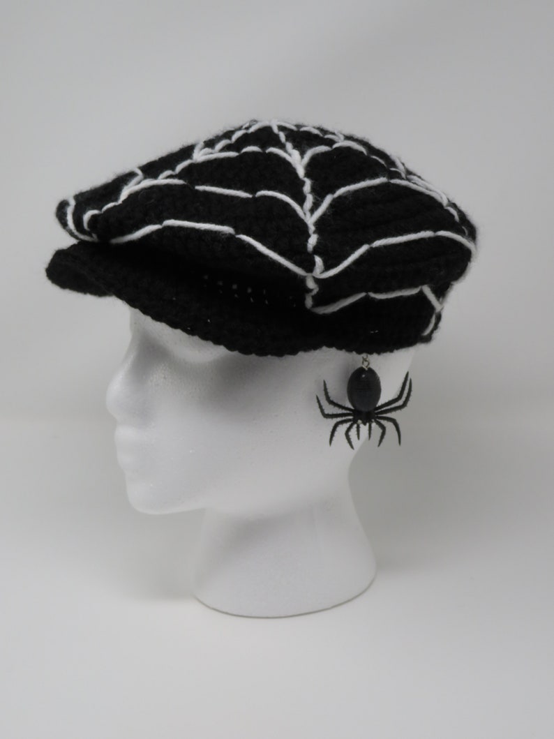 May include: A black crocheted hat with a white spiderweb design. A black spider earring is hanging from the hat.