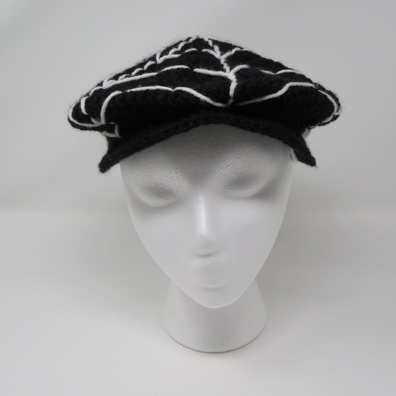 May include: A black and white knitted newsboy cap with a white spiderweb design.