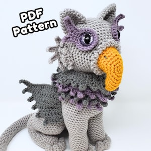May include: Crocheted griffin plushie in shades of gray, purple, and yellow. The handmade creature features a bird-like beak, large eyes, and detailed wings. The text "PDF Pattern" is visible in the upper left corner.