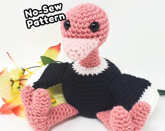 May include: A crocheted vulture plush toy with a pink head and feet, a black body, and white wing tips. The text No-Sew Pattern is visible in the upper left corner. The toy features black plastic eyes and a textured yarn construction.