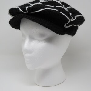 May include: A black and white patterned crocheted newsboy cap. The cap has a white brim and a black crown with a white geometric design.
