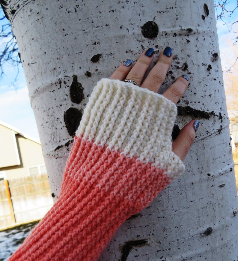 May include: A pair of crocheted fingerless gloves with a two-tone color scheme. The gloves are white at the top and transition to a coral color at the bottom.
