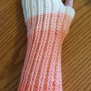 May include: A pair of crocheted arm warmers with a white top and a pink ombre bottom.