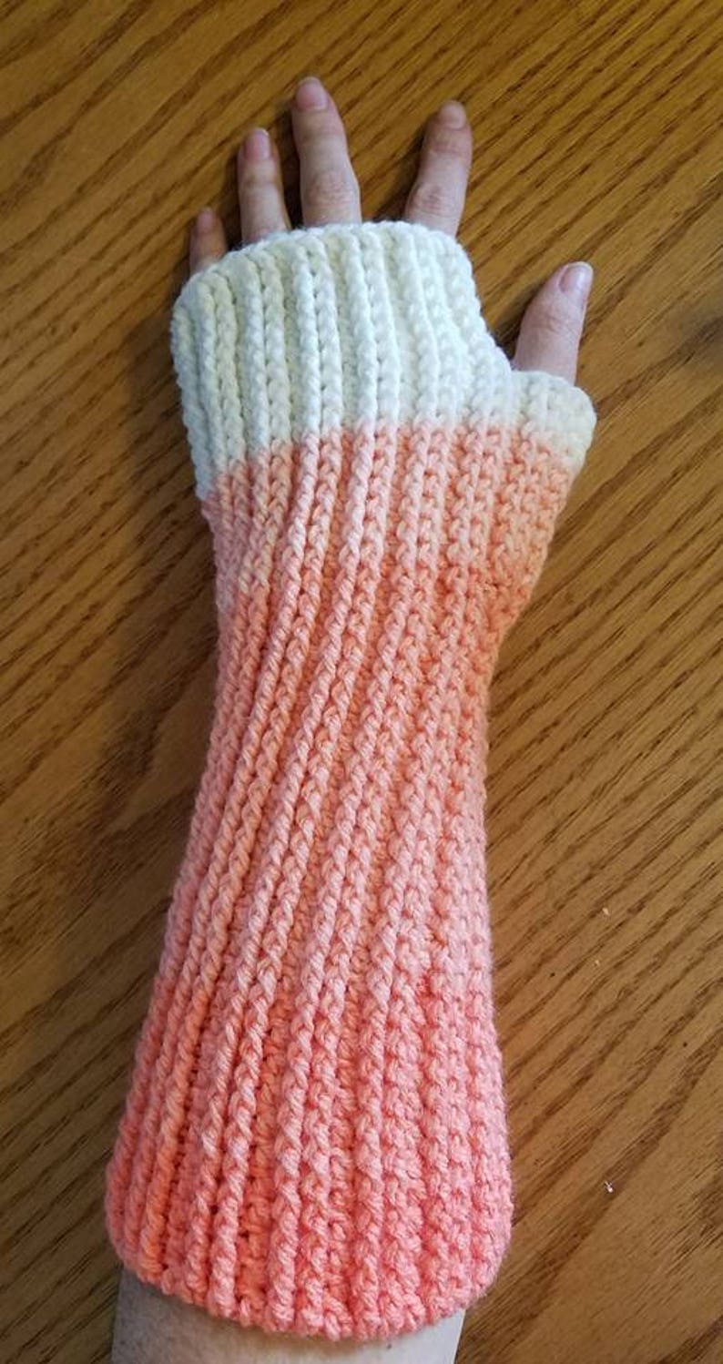 May include: A pair of crocheted arm warmers with a white top and a pink ombre bottom.