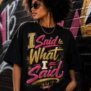 May include: A black short-sleeved t-shirt featuring a graphic print with the text "I Said What I Said" in a stylised font. The lettering combines metallic gold and vibrant pink colours with a distressed, textured effect and a small crown icon.