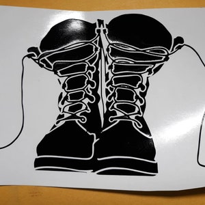 May include: Black and white graphic of two combat boots with laces. The boots are depicted in a silhouette style, with detailed lacing and a rugged design. The image is on a white background.