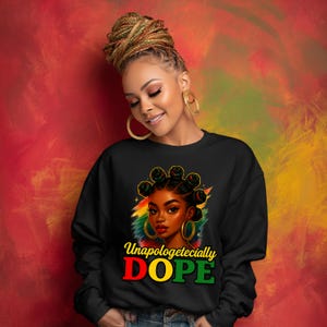 May include: Black sweatshirt featuring a vibrant illustration of a woman with braided hair and gold hoop earrings. The design includes the text "Unapologetically DOPE" in red, yellow, and green, set against a colorful background. The woman is smiling.