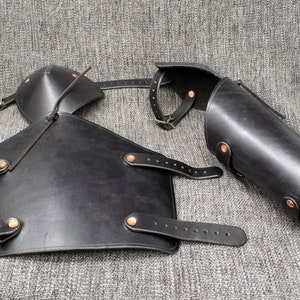 May include: Black leather arm guards with straps and buckles. The guards are designed to protect the forearms and elbows.