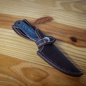 May include: A brown leather knife sheath with a snap closure and a blue and black patterned knife inside.