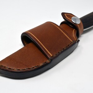 May include: A brown leather knife sheath with a snap closure and a light brown stitching detail.