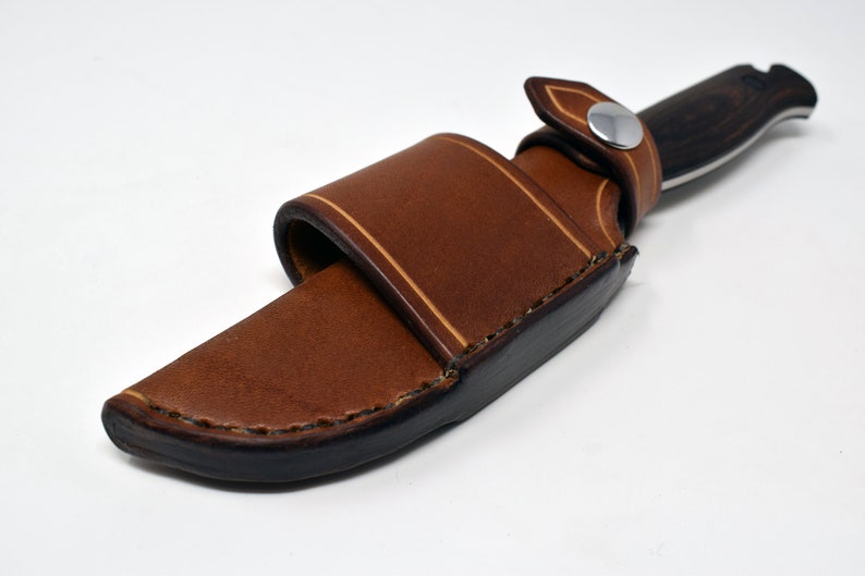 May include: A brown leather knife sheath with a snap closure and a light brown stitching detail.