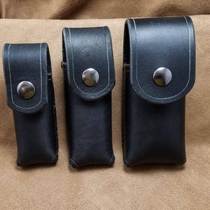May include: Three black leather cases with silver snaps. The cases are different sizes and are lined with a light green material.