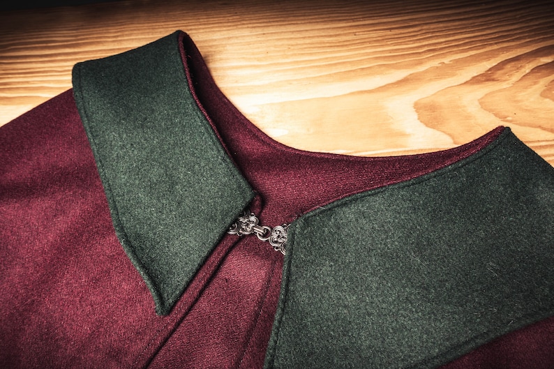 Puede incluir: Primer plano de una prenda de lana color burdeos y verde con un cierre met&aacute;lico decorativo. La prenda tiene un cuello con un borde puntiagudo.