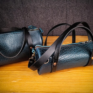 Puede incluir: Dos bolsos de cuero azul con correas negras. El bolso m&aacute;s grande tiene dos asas y el bolso m&aacute;s peque&ntilde;o tiene una sola correa. Ambos bolsos tienen un forro azul claro.
