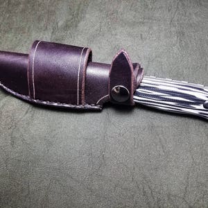 May include: A black and white patterned knife with a brown leather sheath.