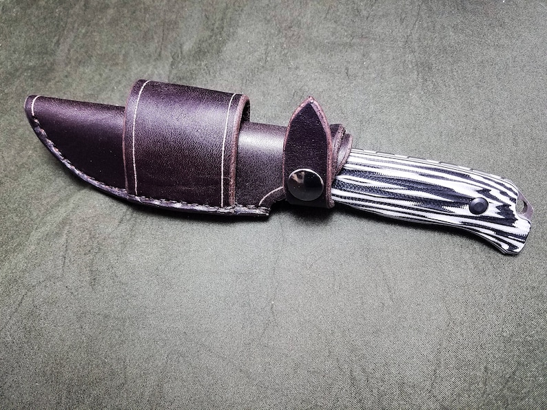 May include: A black and white patterned knife with a brown leather sheath.