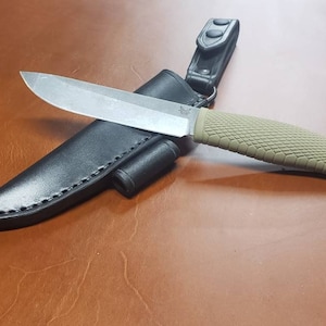 Peut inclure: Un couteau à manche brun avec une poignée texturée beige, dans un étui en cuir noir.