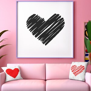 May include: A pink sofa with two throw pillows featuring red heart designs. A framed print with a black hand-drawn heart design hangs on the wall behind the sofa.