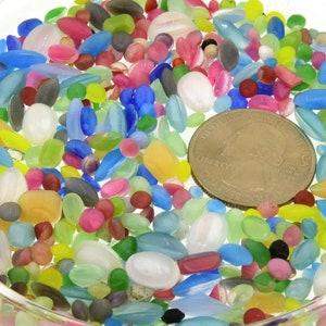 May include: A glass dish filled with a variety of colorful glass beads and a US quarter for scale.