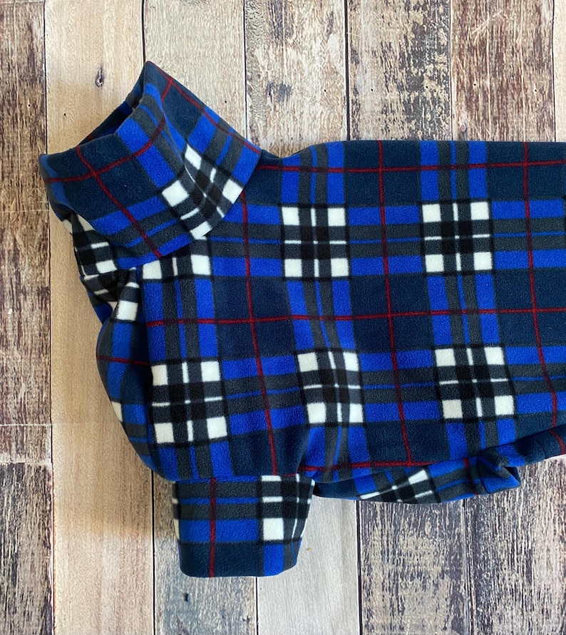 May include: A blue plaid dog sweater with a high collar and sleeves. The pattern includes navy, red, white, and gray squares and lines. The sweater is made of a soft fleece material.