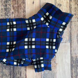 May include: A blue, black, white, and red plaid fleece dog coat. The coat features a classic plaid pattern with a navy blue base, accented by black, white, and red lines. The coat is designed to provide warmth and comfort for dogs.