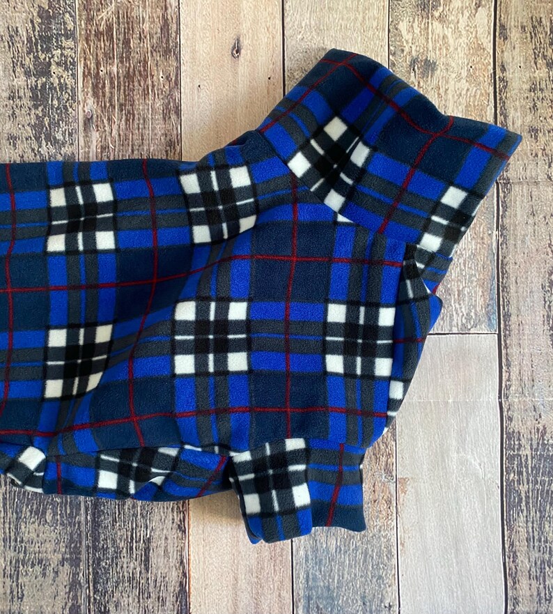 May include: A blue, black, white, and red plaid fleece dog coat. The coat features a classic plaid pattern with a navy blue base, accented by black, white, and red lines. The coat is designed to provide warmth and comfort for dogs.