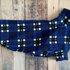 May include: A blue, black, and white plaid dog coat. The coat is made of a soft fleece material and features a classic plaid pattern with red accent lines. The coat is designed to fit a dog and has a collar.