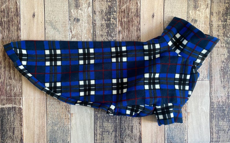 May include: A blue, black, and white plaid dog coat. The coat is made of a soft fleece material and features a classic plaid pattern with red accent lines. The coat is designed to fit a dog and has a collar.