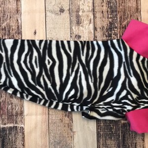 May include: A black and white zebra print dog sweater with a pink collar.